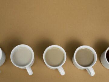 Aesthetic arrangement of coffee mugs with varying milk content on a brown surface, viewed from above.