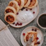 Cozy breakfast scene featuring traditional syrniki with cranberries, yogurt, and a hot cup of coffee.