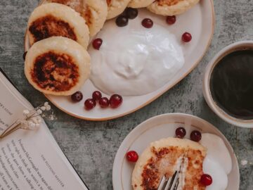 Cozy breakfast scene featuring traditional syrniki with cranberries, yogurt, and a hot cup of coffee.