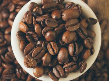 High-quality close-up image of roasted coffee beans in a cup on a wooden table.