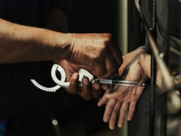 Close-up view of a person being handcuffed in a jail setting, focusing on hands and handcuffs.