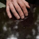 Close-up of a hand touching a rain-dappled surface, symbolizing loss and reflection.