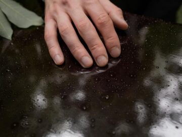 Close-up of a hand touching a rain-dappled surface, symbolizing loss and reflection.