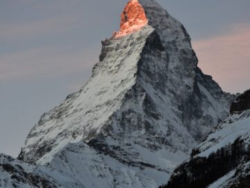 Stunning view of the snowcapped Matterhorn at sunrise, illuminating the peak in a warm glow, Zermatt, Switzerland.