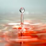 Macro capture of a droplet splash on a surface with a reflection and colored water effect, creating an artistic view.