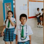 Children wearing school uniforms inside a classroom, engaged in conversations.