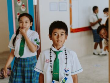 Children wearing school uniforms inside a classroom, engaged in conversations.