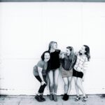 Four young women laughing together in front of an urban door, showcasing friendship and happiness.