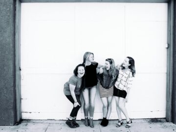 Four young women laughing together in front of an urban door, showcasing friendship and happiness.