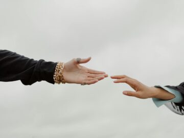 Close-up of two hands reaching for each other under a cloudy sky, symbolizing connection.
