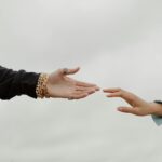Close-up of two hands reaching for each other under a cloudy sky, symbolizing connection.