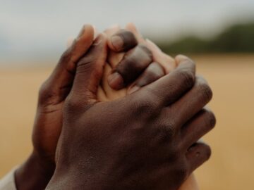 A close-up of two people of different ethnicities holding hands outdoors, symbolizing unity and support.