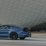 Blue Ford Mustang parked on roadside with geometric background. Modern car photography.
