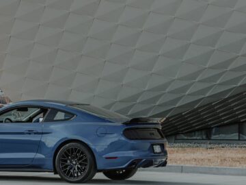 Blue Ford Mustang parked on roadside with geometric background. Modern car photography.