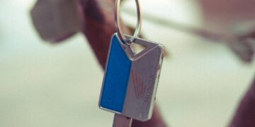 A close-up shot of a key with a leather strap hanging from a tree branch.
