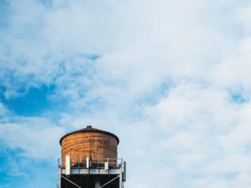 A vintage water tank on a building rooftop with a bright blue cloudy sky in the background.