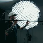 Cameraman adjusts lighting equipment on film set. Behind-the-scenes production view.