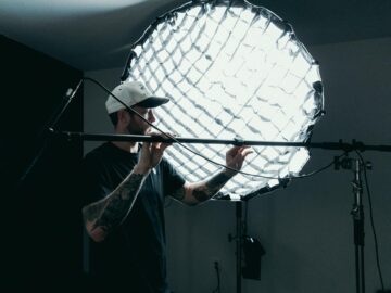 Cameraman adjusts lighting equipment on film set. Behind-the-scenes production view.