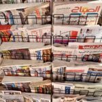 A diverse collection of newspapers in various languages displayed on a metal stand.