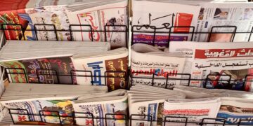 A diverse collection of newspapers in various languages displayed on a metal stand.