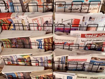 A diverse collection of newspapers in various languages displayed on a metal stand.