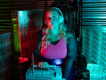 Woman with headphones and radio sitting amidst stacks of dollar bills.
