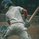 A young male cricketer wearing full gear, ready to bat on an outdoor field.