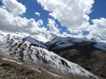 Serene snow-covered mountains under a clear blue sky with fluffy white clouds.