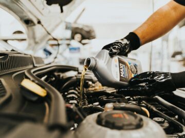 Close-up of a mechanic pouring engine oil into a car engine in an auto repair shop.