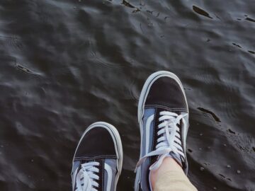 Casual black sneakers dangling above water, capturing a relaxed moment by the sea in İstanbul.