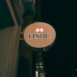 Vertical shot of an HSBC bank sign lit up at night, showcasing urban bank architecture.