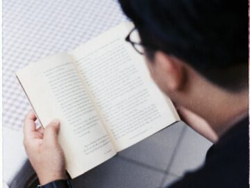 An adult male concentrating on reading a book indoors, creating a serene and intellectual atmosphere.