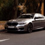 Stylish silver BMW parked on an autumn road surrounded by fallen leaves.