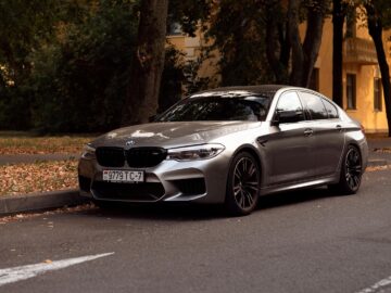 Stylish silver BMW parked on an autumn road surrounded by fallen leaves.