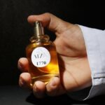 Close-up of a hand holding a perfume bottle with shadowed backdrop, emphasizing elegance.