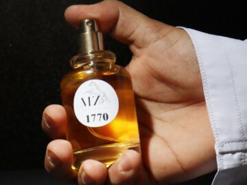 Close-up of a hand holding a perfume bottle with shadowed backdrop, emphasizing elegance.