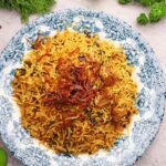 An appetizing biryani dish served on a blue and white decorative plate, accompanied by fresh ingredients.