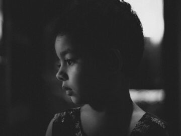 A candid black and white portrait of a thoughtful child in side view.