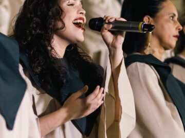 Woman singing with a choir, passionately holding a microphone. Captured in mid-performance with focused expression.