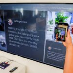 A person uses a smartphone to scan a QR code displayed on a large screen indoors.