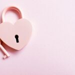 Aesthetic photo of a heart-shaped pink padlock with a matching key on a pink background, perfect for love themes.
