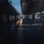 Empty train station platform under a clear blue sky with shadows and sunlight.