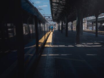 Empty train station platform under a clear blue sky with shadows and sunlight.