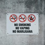 A clear warning sign prohibiting smoking, vaping, and marijuana on a concrete wall.