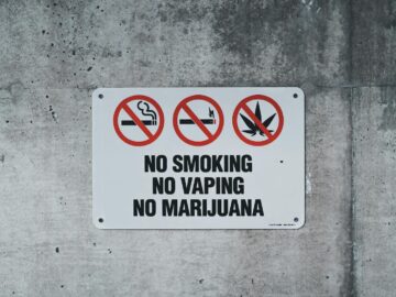 A clear warning sign prohibiting smoking, vaping, and marijuana on a concrete wall.