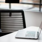A sleek laptop on a white desk in a contemporary office setting with mesh chair.
