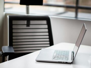 A sleek laptop on a white desk in a contemporary office setting with mesh chair.