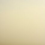 A single sailboat drifts in calm, foggy waters, creating a tranquil and minimalist scene.