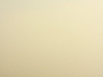 A single sailboat drifts in calm, foggy waters, creating a tranquil and minimalist scene.