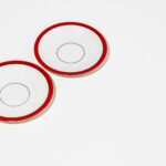 Top view of two white plates with red rims on a white background.